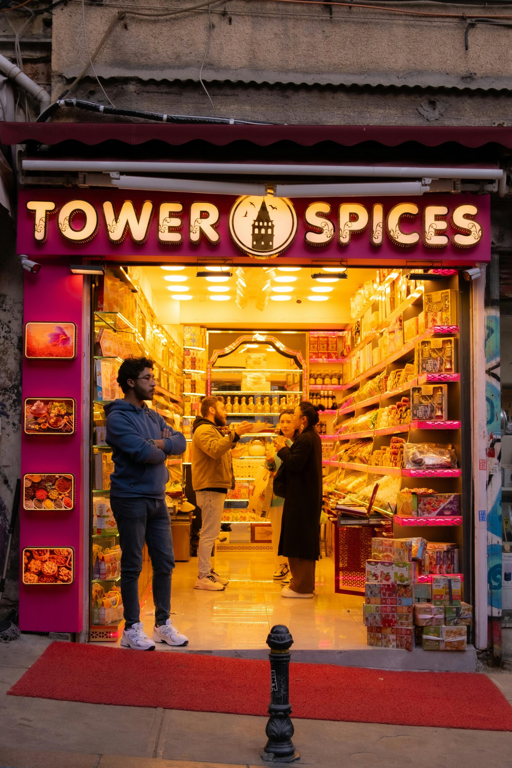Colorful spice shop with people browsing, glowing warmly under evening lights, inviting atmosphere.
